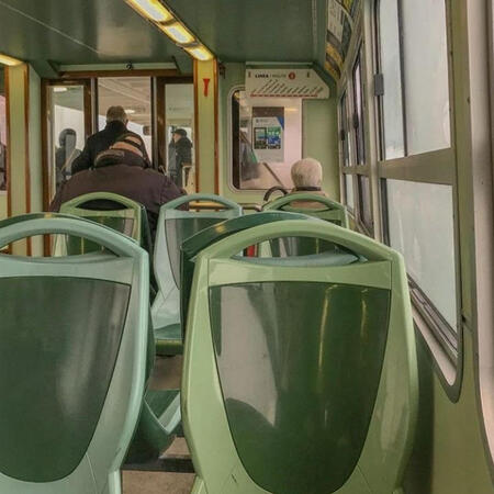 A front-facing bus interior from the POV of a window seat. The colors are light shades of green.