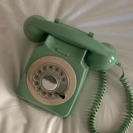 A sage green rotary phone sitting atop white silk sheets