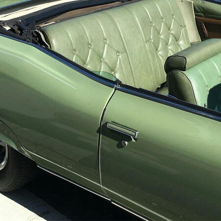 The side of a vintage convertible car. It is a very light green, with textured leather seats.